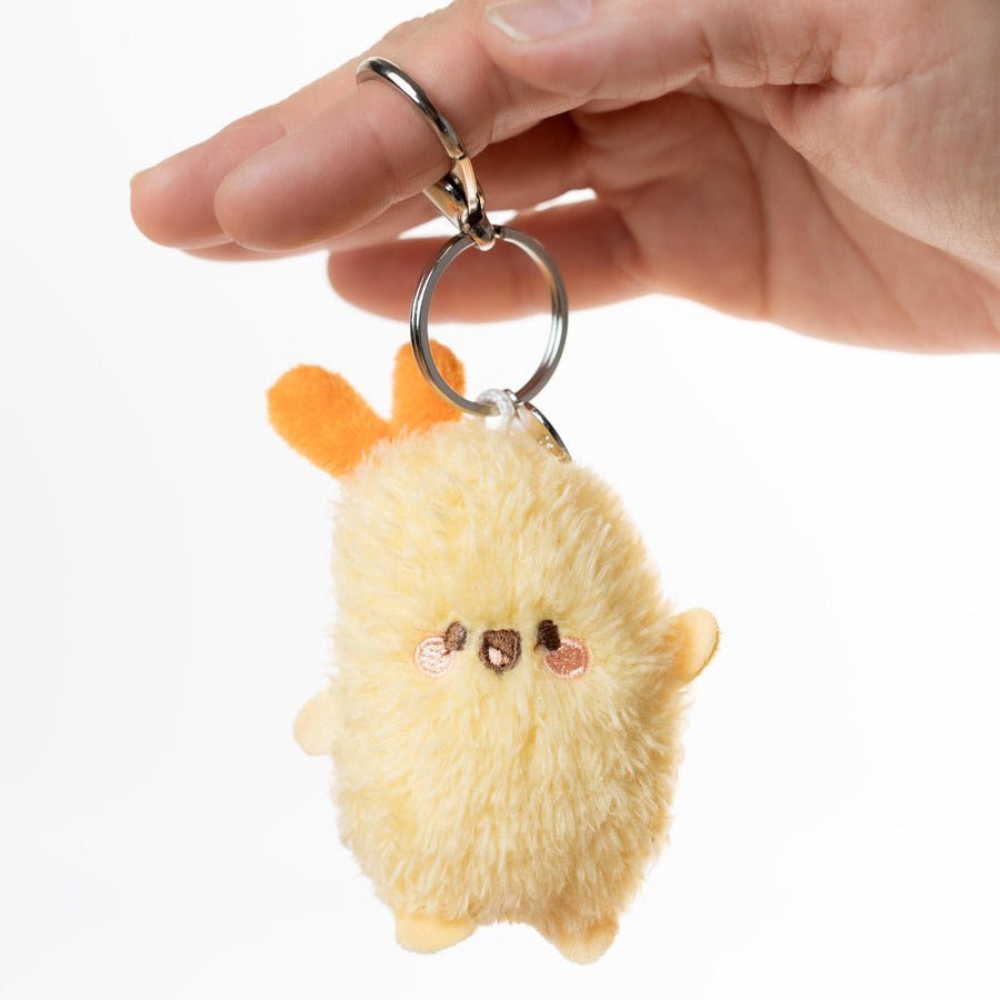 A hand holding a small fluffy plush keychain charm with a silver key ring, against a plain white background.