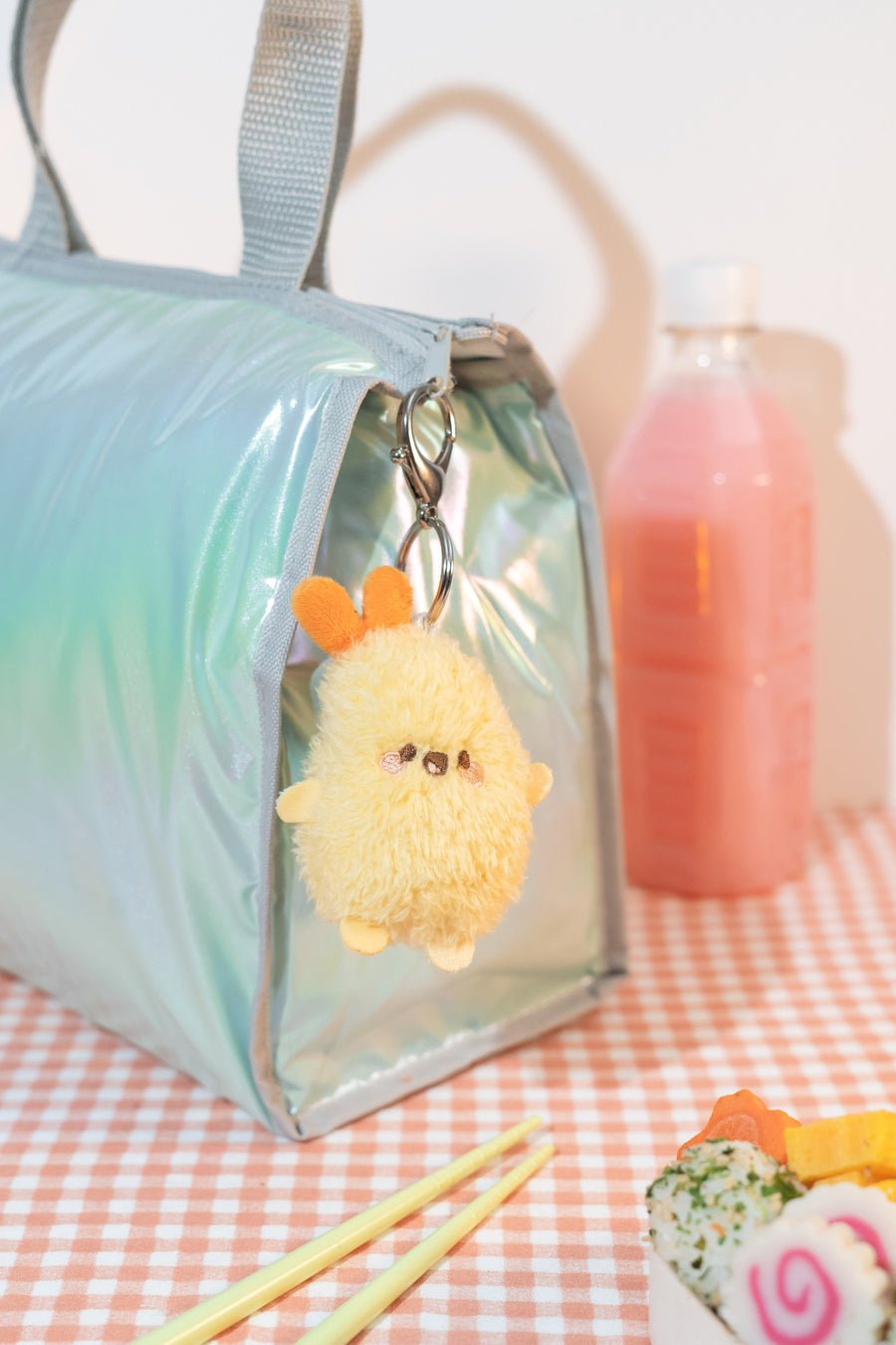 Light blue bag with a fluffy yellow keychain on a checkered tablecloth.