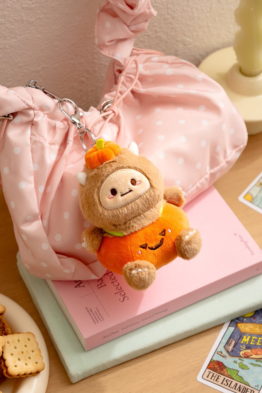 Plush keychain in a Halloween costume on a pink surface with a pink bag in the background.