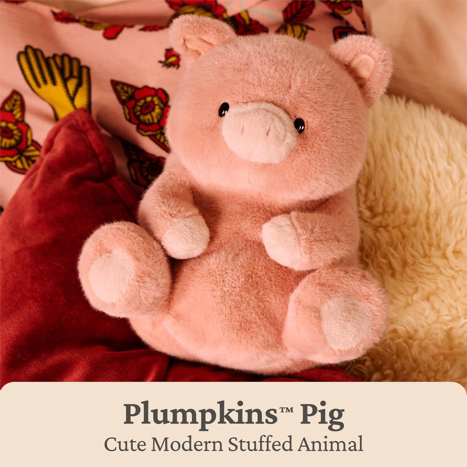 A pink plush stuffed pig toy with small black eyes and a pale pink snout, posed on red and cream textured cushions with a printed fabric background. Text at the bottom reads 'Plumpkins™ Pig' and 'Cute Modern Stuffed Animal'.