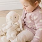 Child in a pink sweater with a plush toy on a light wooden floor.