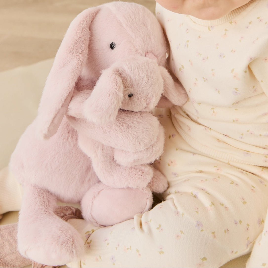 Baby holding pink plush bunny wearing floral patterned pajamas.